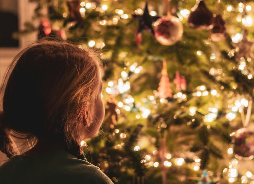 child looking at christmas tree with warm string lights